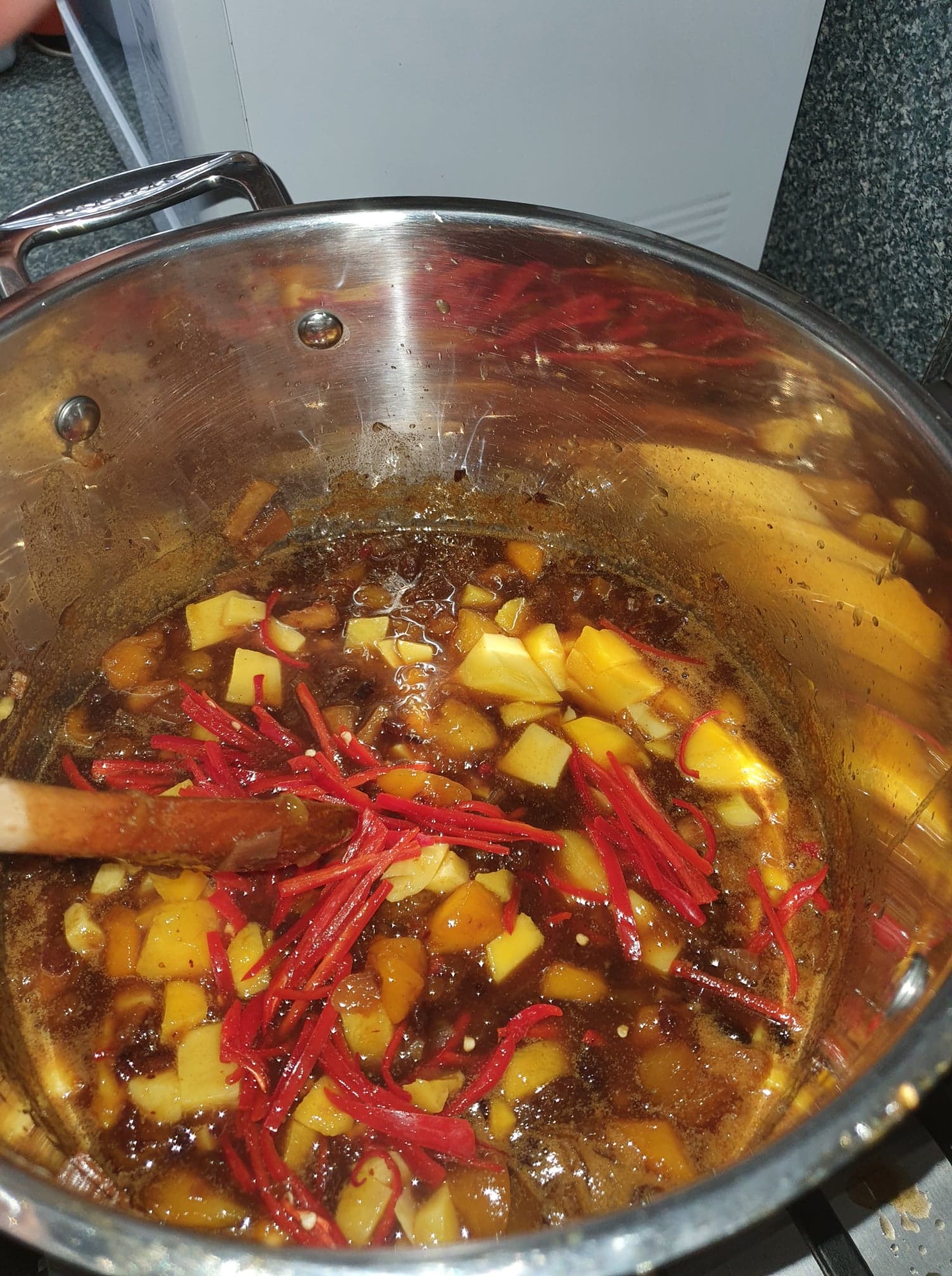 Strips of red chilli and fresh mango cubes stirred into the simmering chutney with a wooden spoon