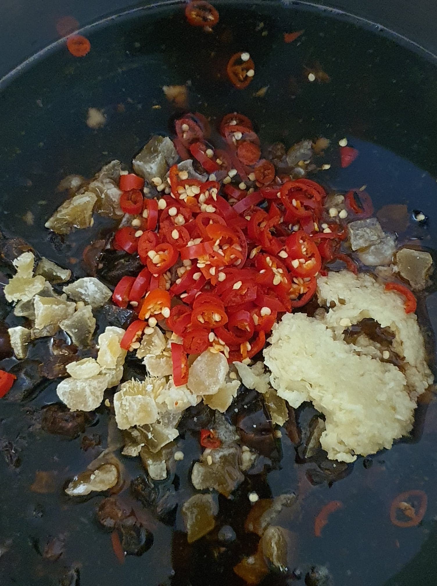 Sliced red chillies, crystallised ginger and grated ginger added to the dark liquid in the cooking pot