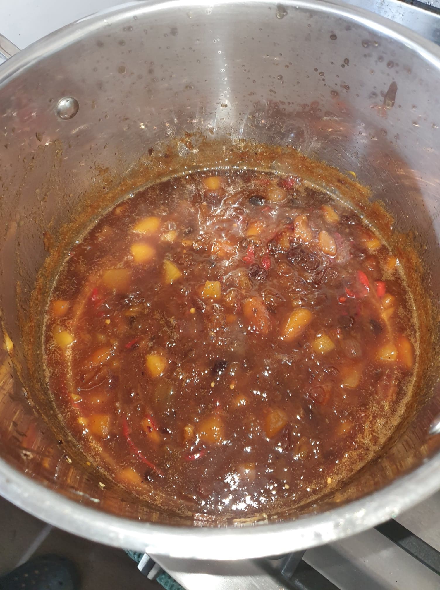 Thickened chutney in a stainless steel pot, with chunks of mango and strips of chilli through the dark glossy sauce